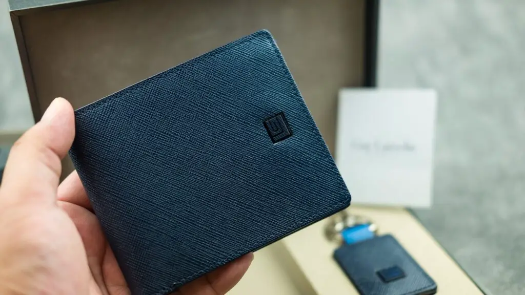 Hand holding a black leather wallet in a gift box